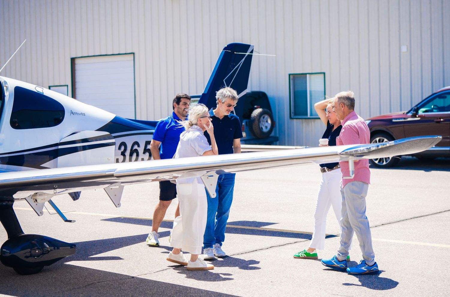 Small aircraft parked on tarmac with people gathered around outside hangar.