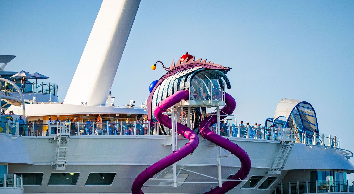 Vibrant purple water slide spiraling on a modern cruise ship deck with passengers enjoying the attraction.
