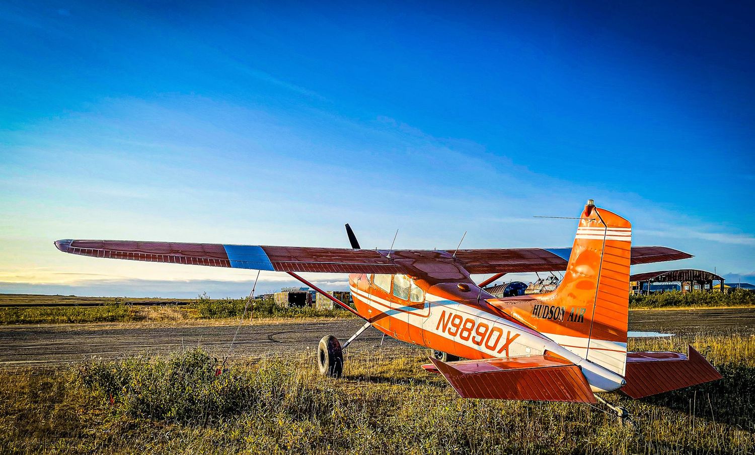 Orange and white small aircraft parked on remote Alaskan tundra landscape.