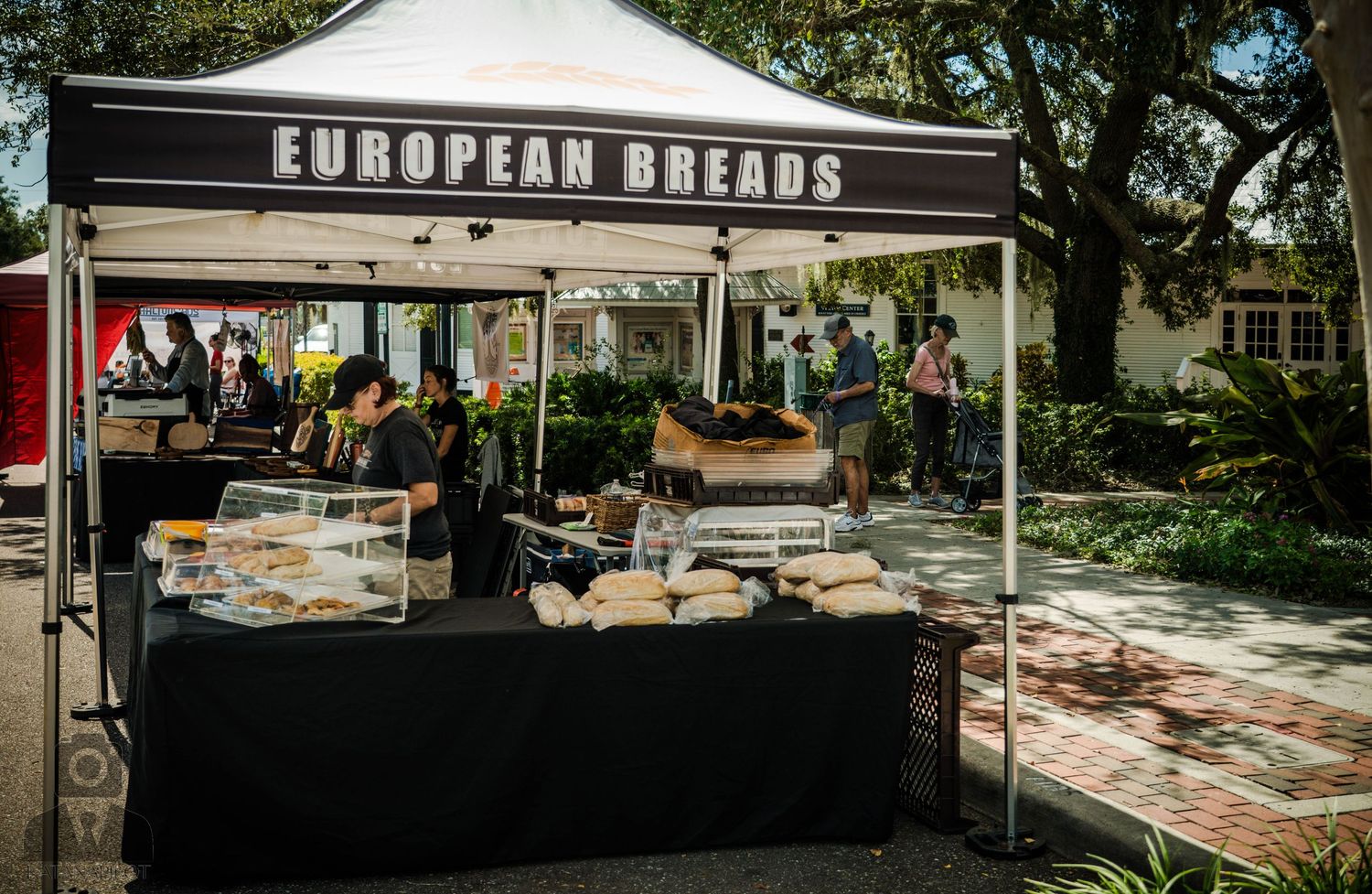 European breads vendor stall with black tablecloth and white canopy at outdoor market.