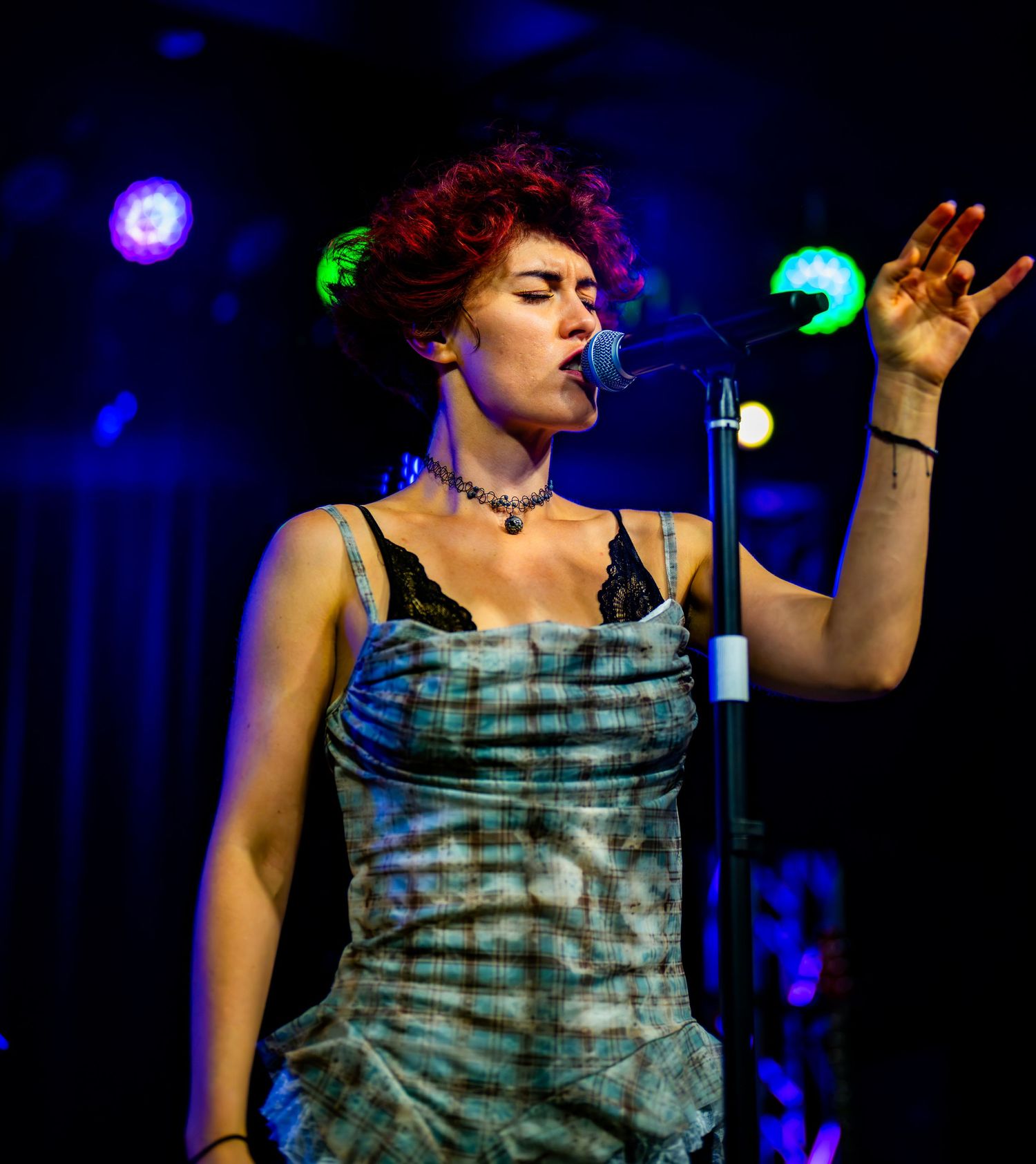 Red-haired female singer raising her hand while performing at a live music concert.