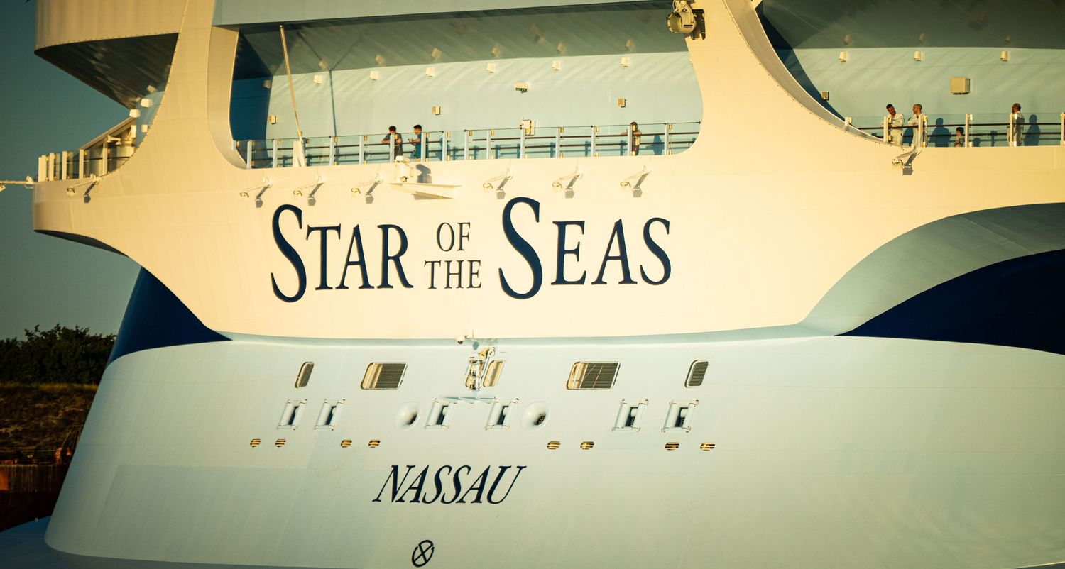 A cruise ship named Star of the Seas docked at port during sunset with warm lighting illuminating its exterior.