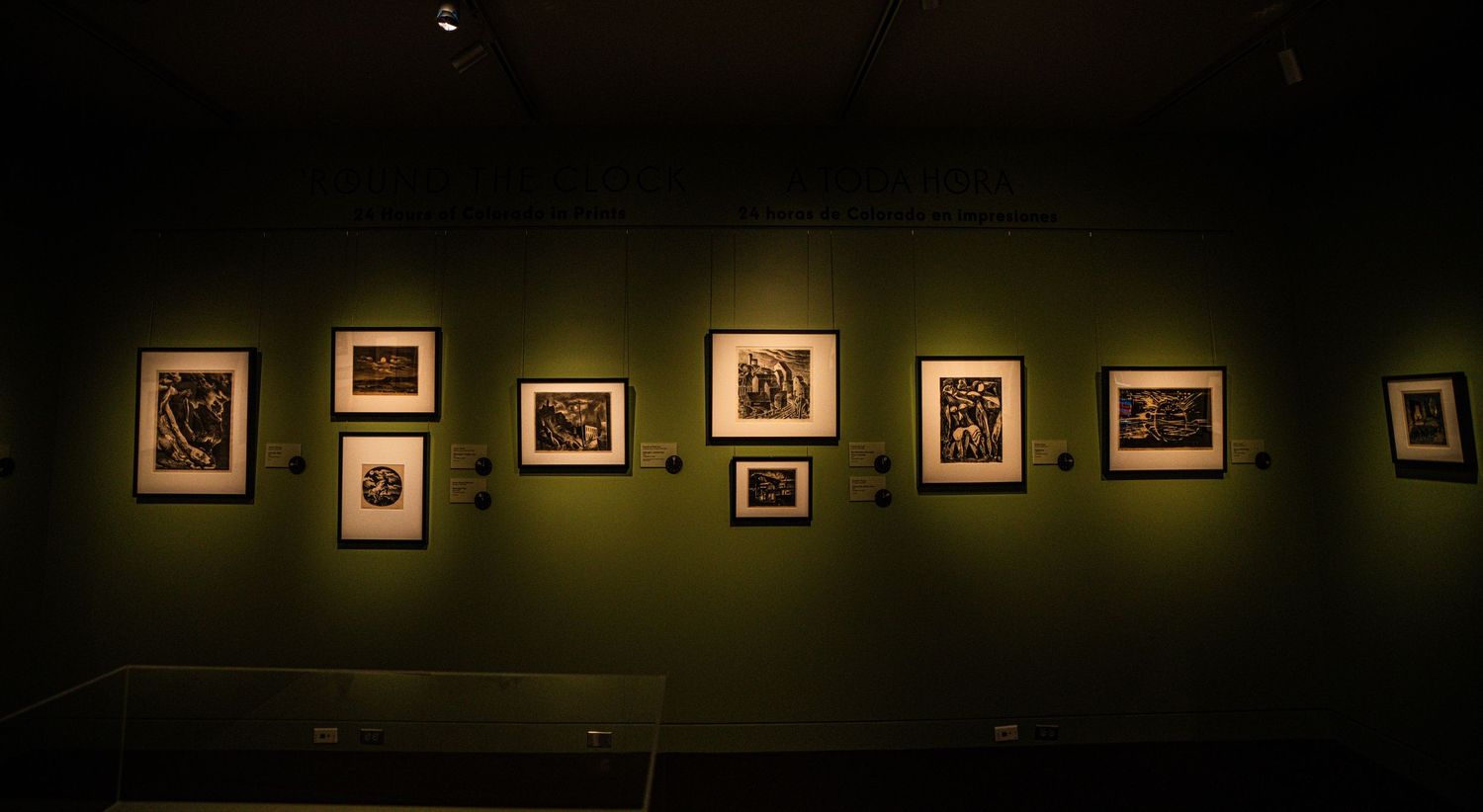 A series of framed photographs displayed in a dark gallery with dim lighting and green walls.