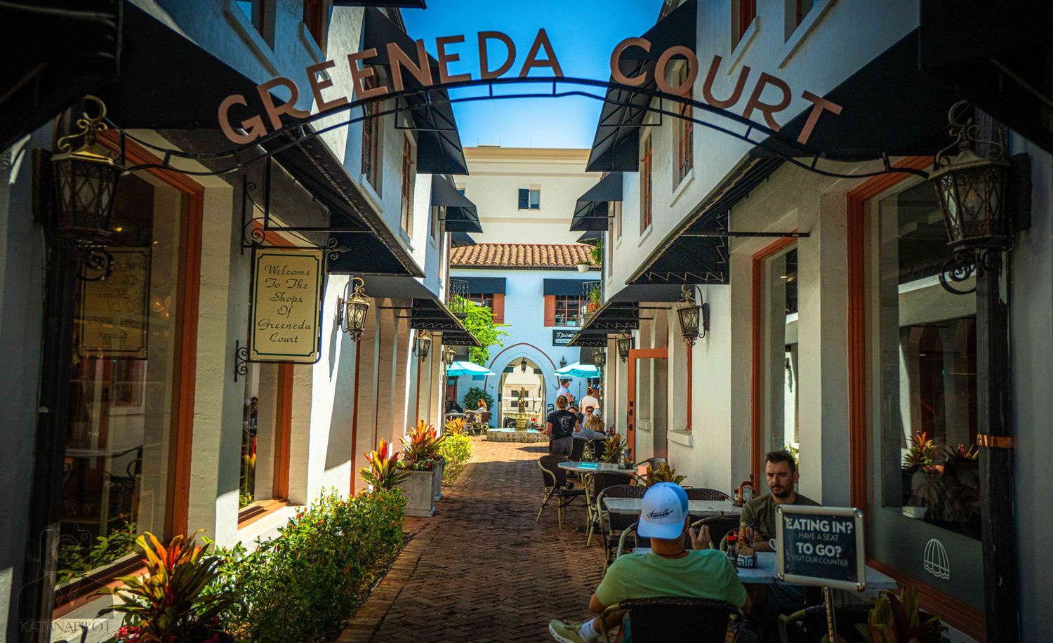 A long covered walkway with white columns and Spanish colonial architecture extends down a historic shopping arcade.