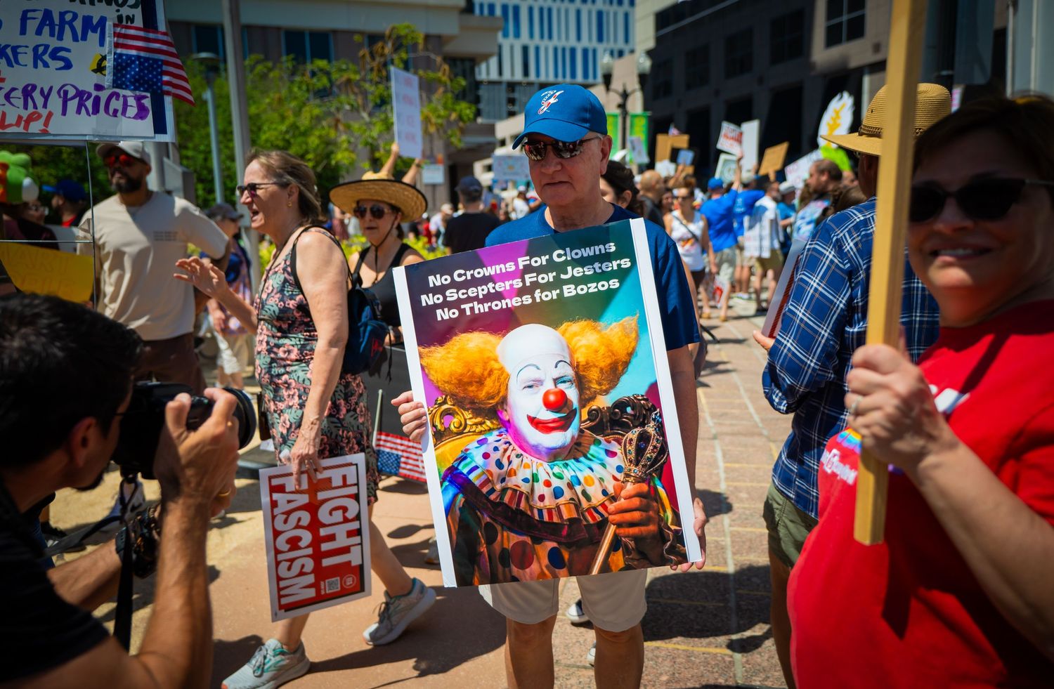 Crowd of demonstrators gather at a protest holding various signs and banners in an outdoor setting.
