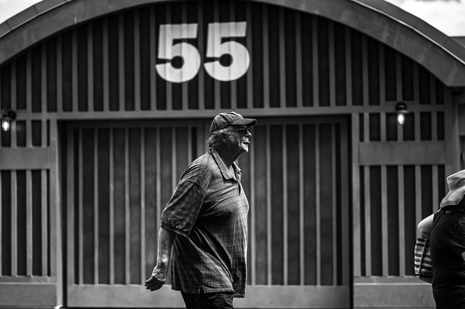 A black and white photo shows a person walking past a large number 53 painted on an industrial wall.