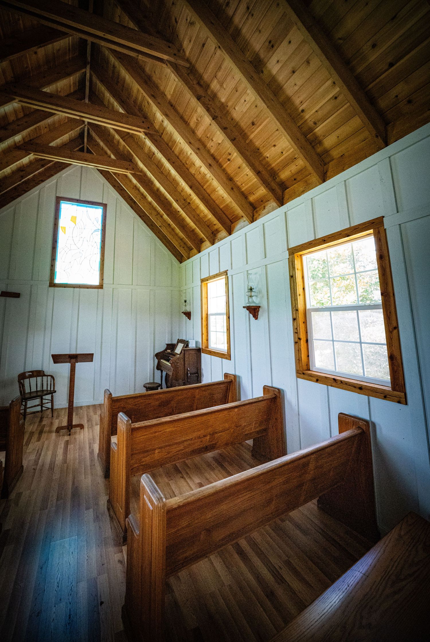 Interior of a rustic chapel with wooden pews and exposed beam ceiling featuring stained glass windows.