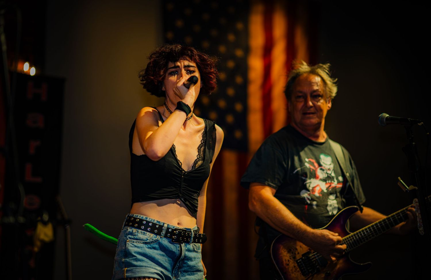 Rock band performs energetically on stage with American flag in background.