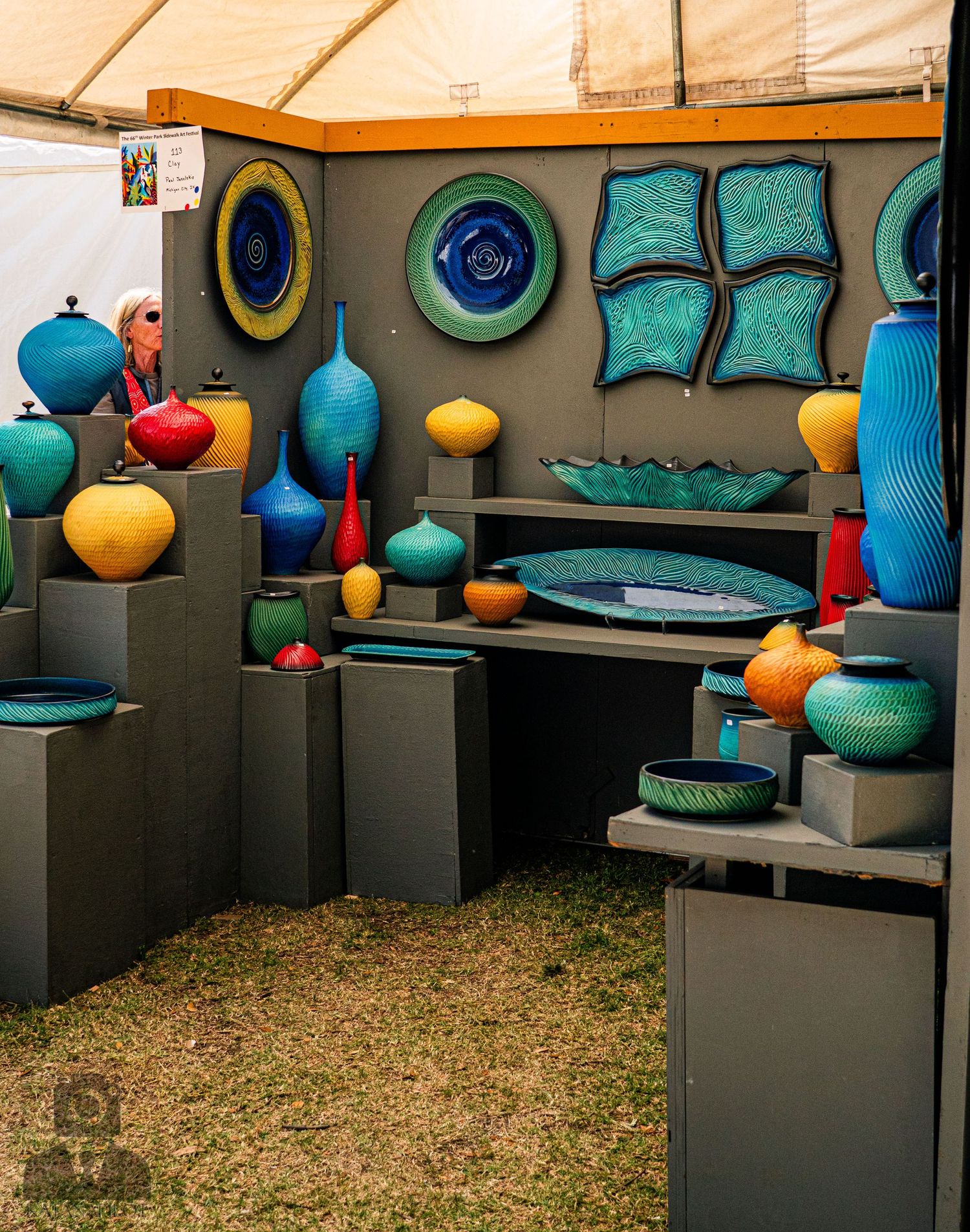 Ceramic pottery display featuring turquoise and orange vessels on black pedestals.
