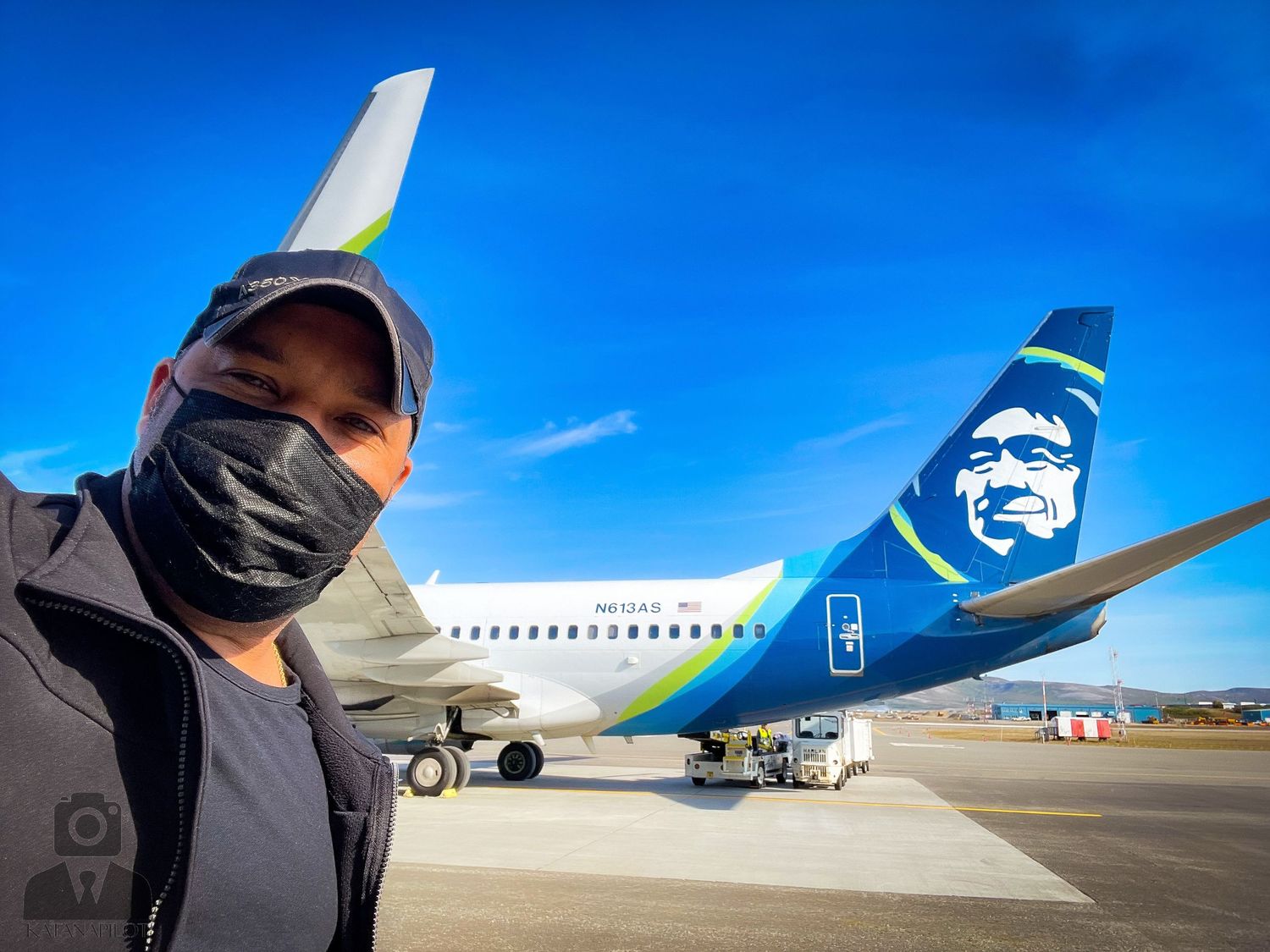 Alaska Airlines plane tail and fuselage on airport tarmac under blue sky.
