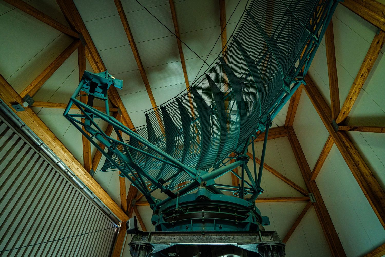 Large green radio telescope dish and steel support structure inside a domed observatory with a wooden beam ceiling.