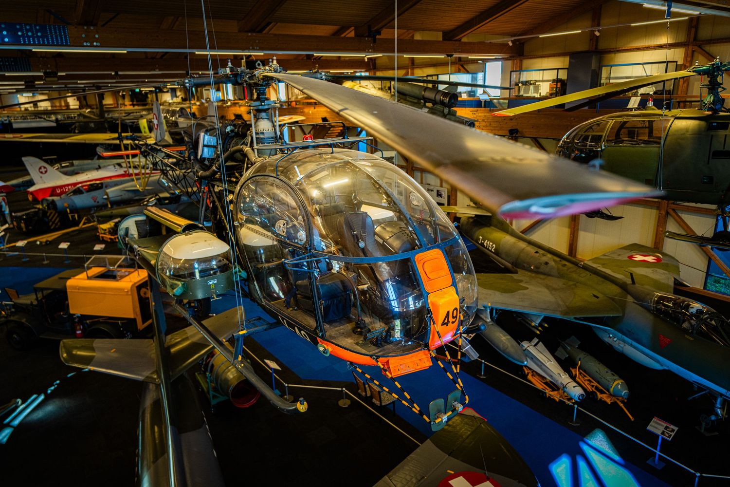 Vintage bubble-canopy helicopter with an orange tail section on display among other historic aircraft in an indoor aviation museum.