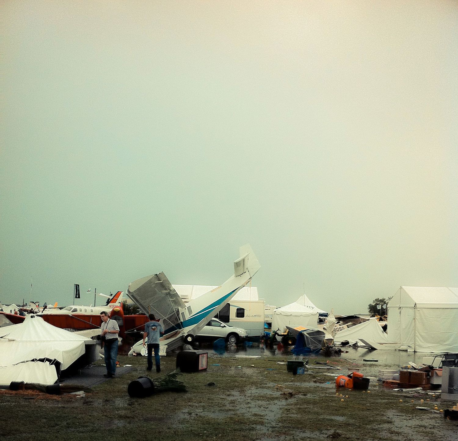 A row of white tents and temporary shelters set up in a disaster relief camp under an overcast sky.