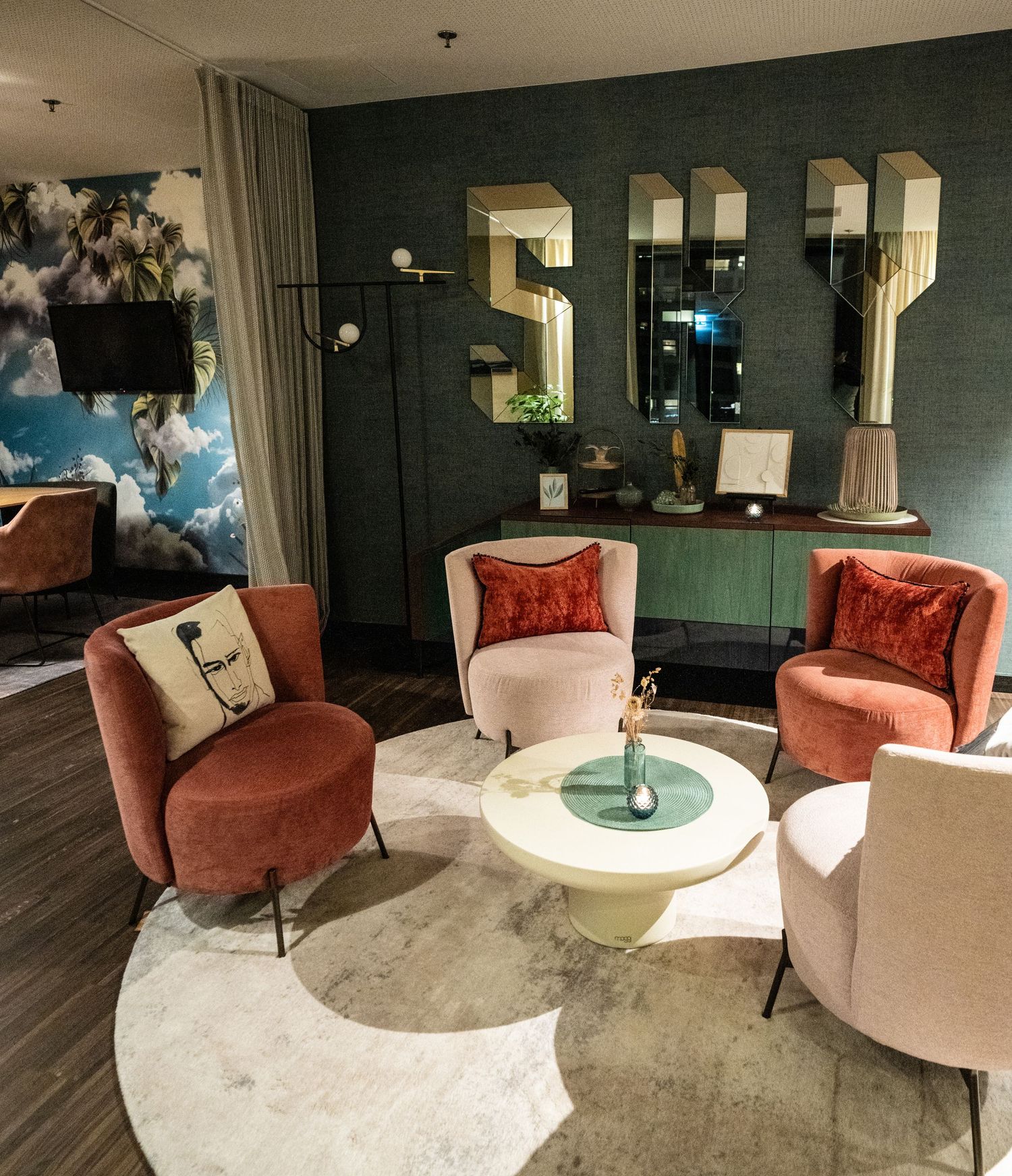 Modern hotel lounge area with coral and beige velvet armchairs arranged around small white side tables.
