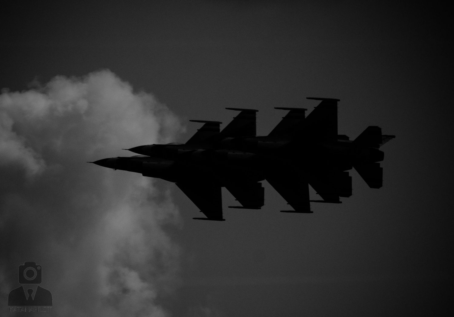 Two military fighter jets fly in close formation against a dramatic cloudy sky in a striking black and white photograph.
