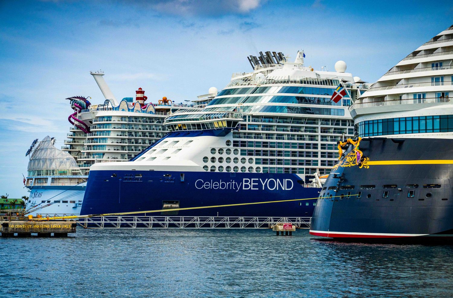 Celebrity Beyond cruise ship docked at port alongside other large cruise ships under a partly cloudy sky.