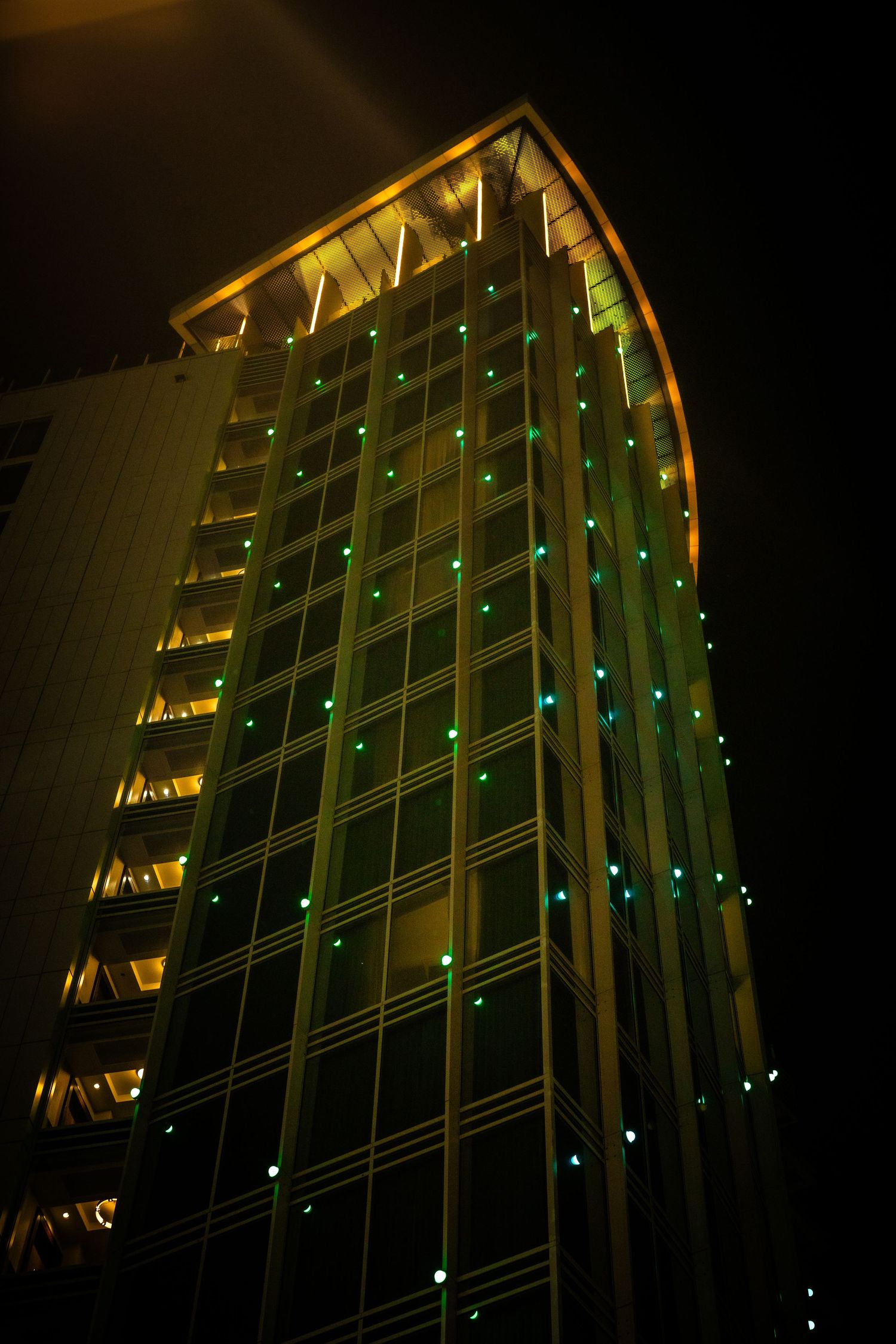 Modern office building exterior lit with yellow and green lights at night.