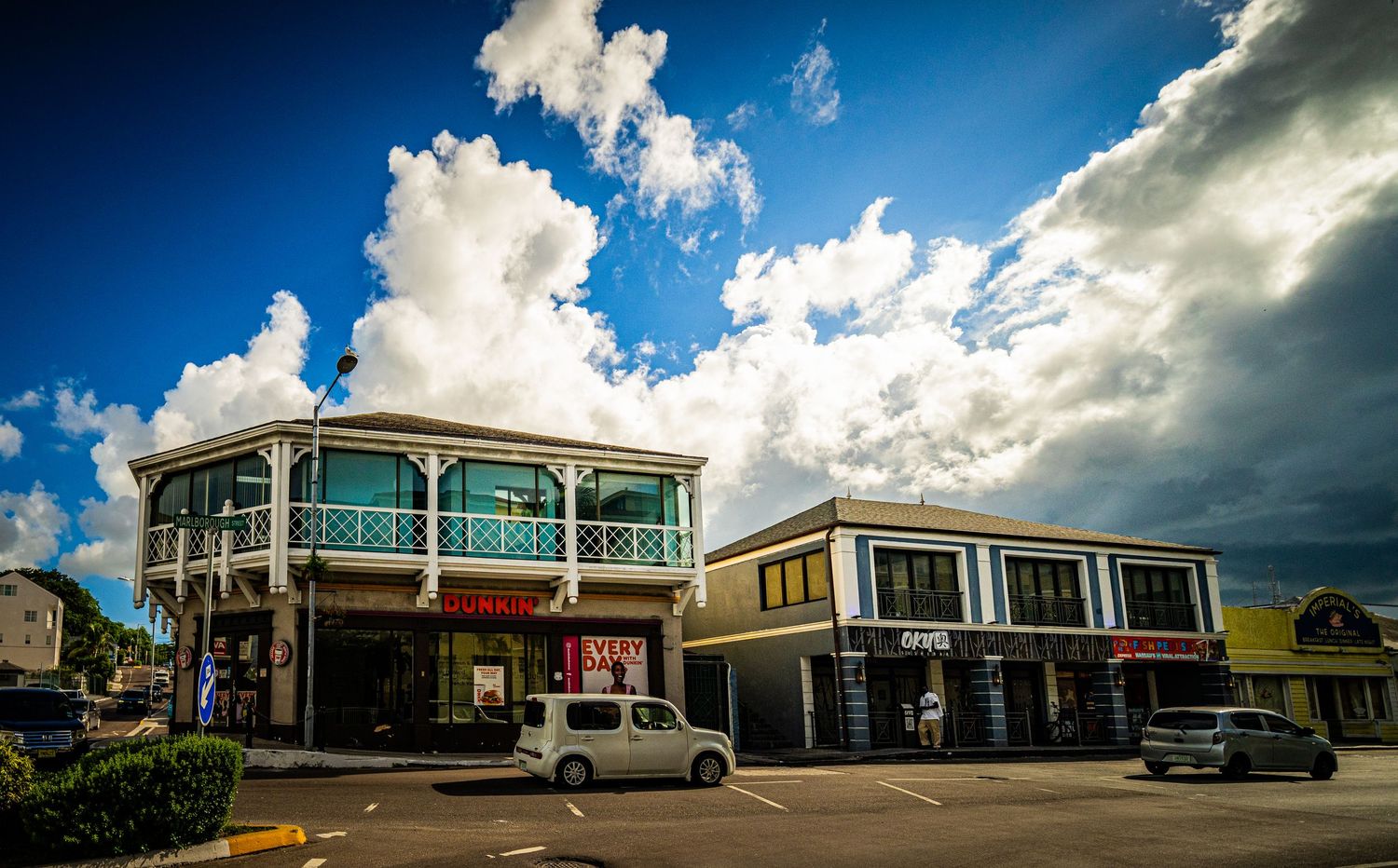 Colorful Caribbean commercial buildings under dramatic blue sky with white clouds in a tropical town center.