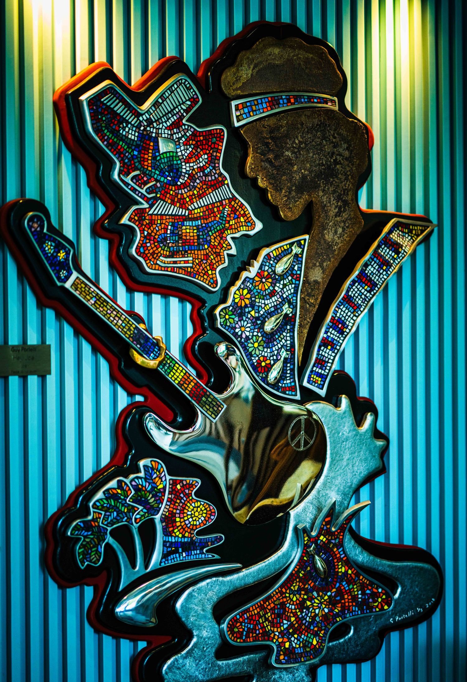 Colorful mosaic art sculpture of Jimi Hendrix playing guitar with vibrant beaded details on blue background.