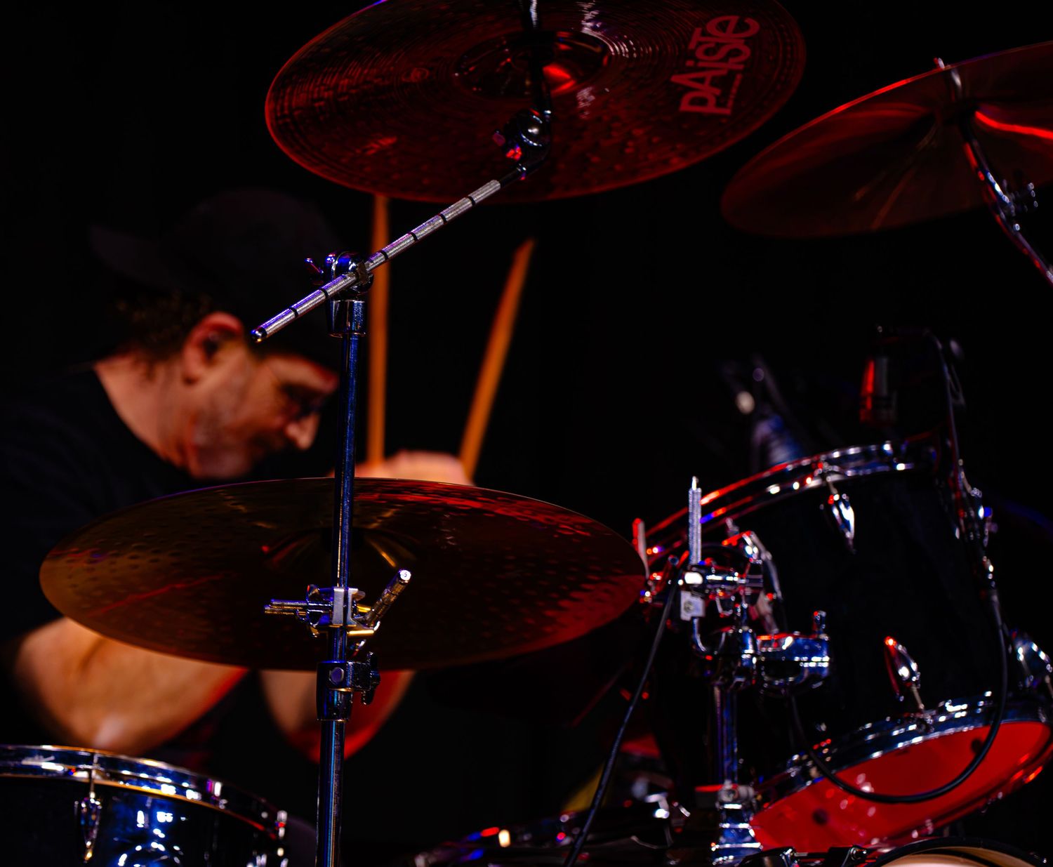 Drummer performing live on stage with cymbals and drum kit under red stage lighting.