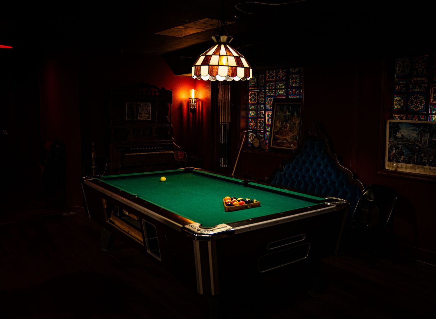 A dimly lit pool table in a cozy bar setting with warm lighting and vintage decor creates an inviting atmosphere.