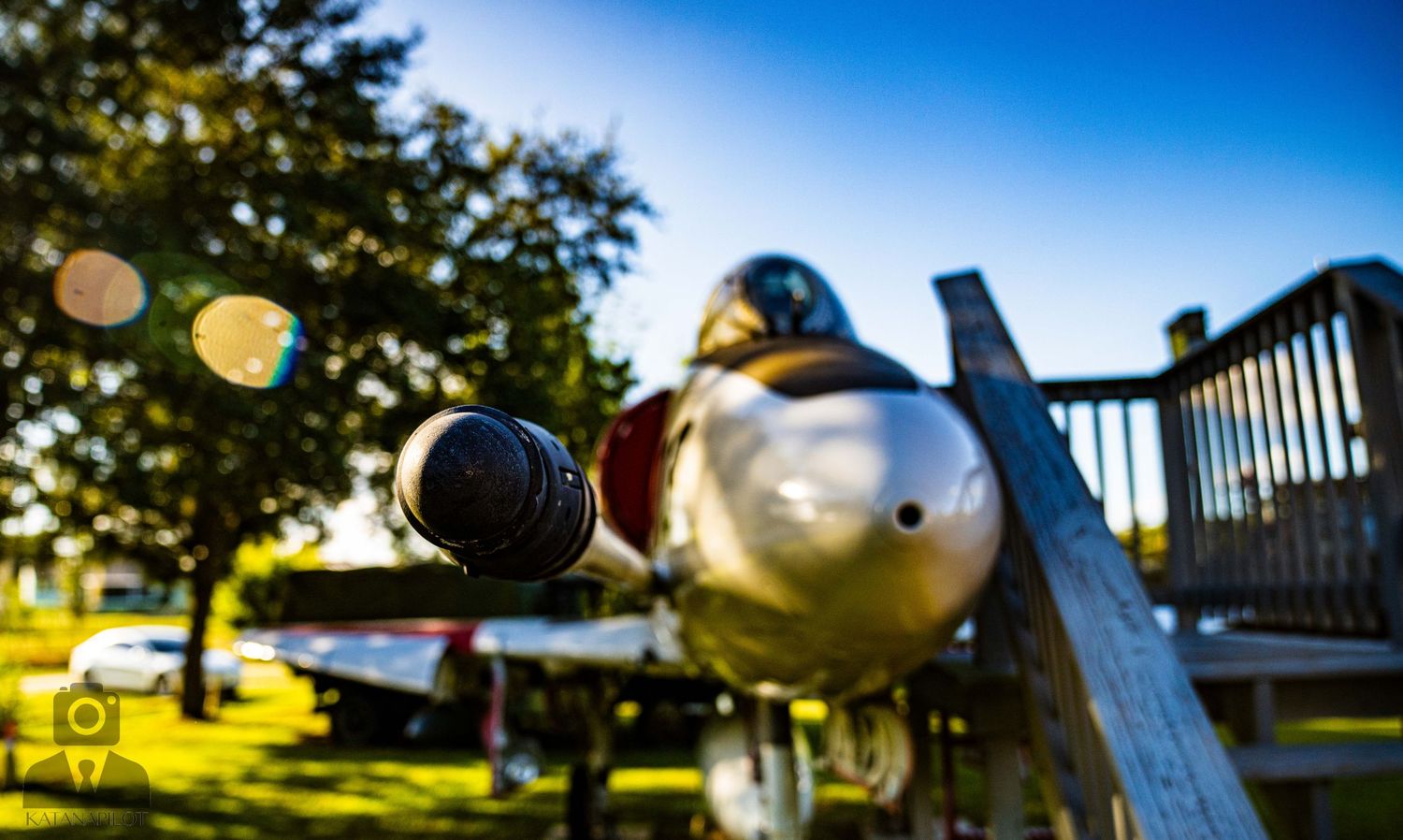 Military aircraft exhibits arranged outdoors against a vivid blue sky with sunlight filtering through trees.