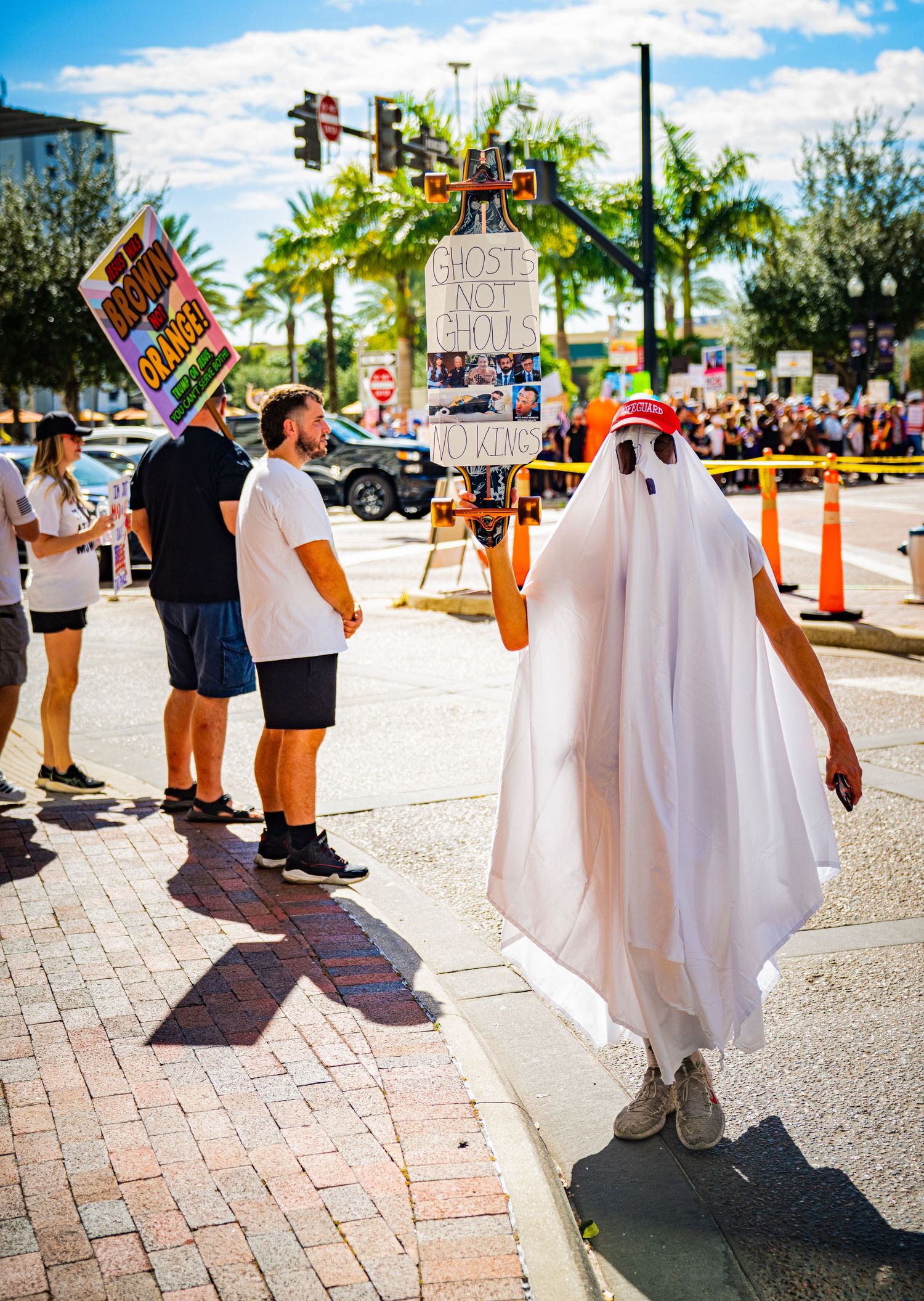 People in ghost costumes with protest signs standing on a sunny sidewalk.