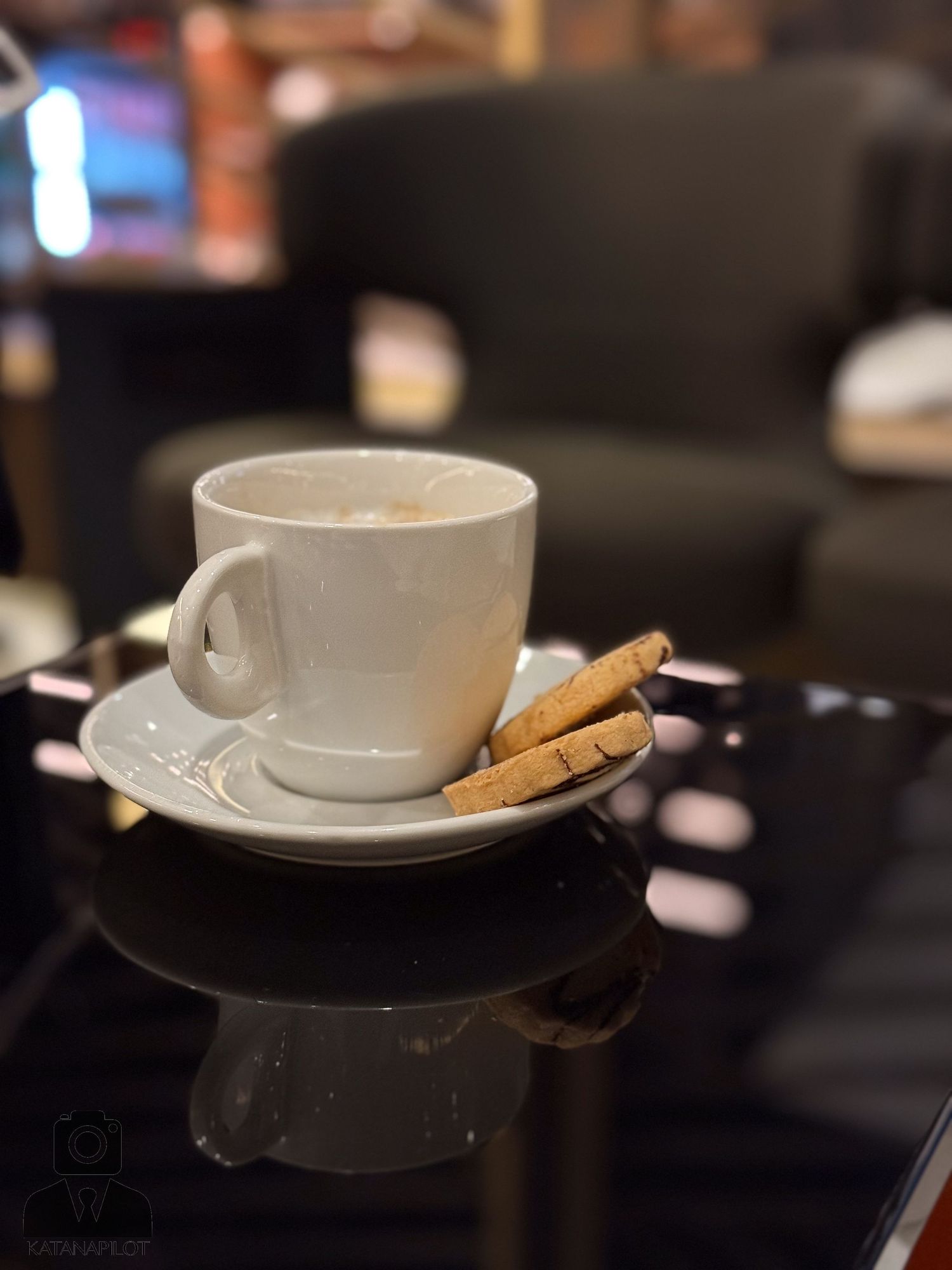 White coffee cup with saucer and biscotti on dark reflective surface.