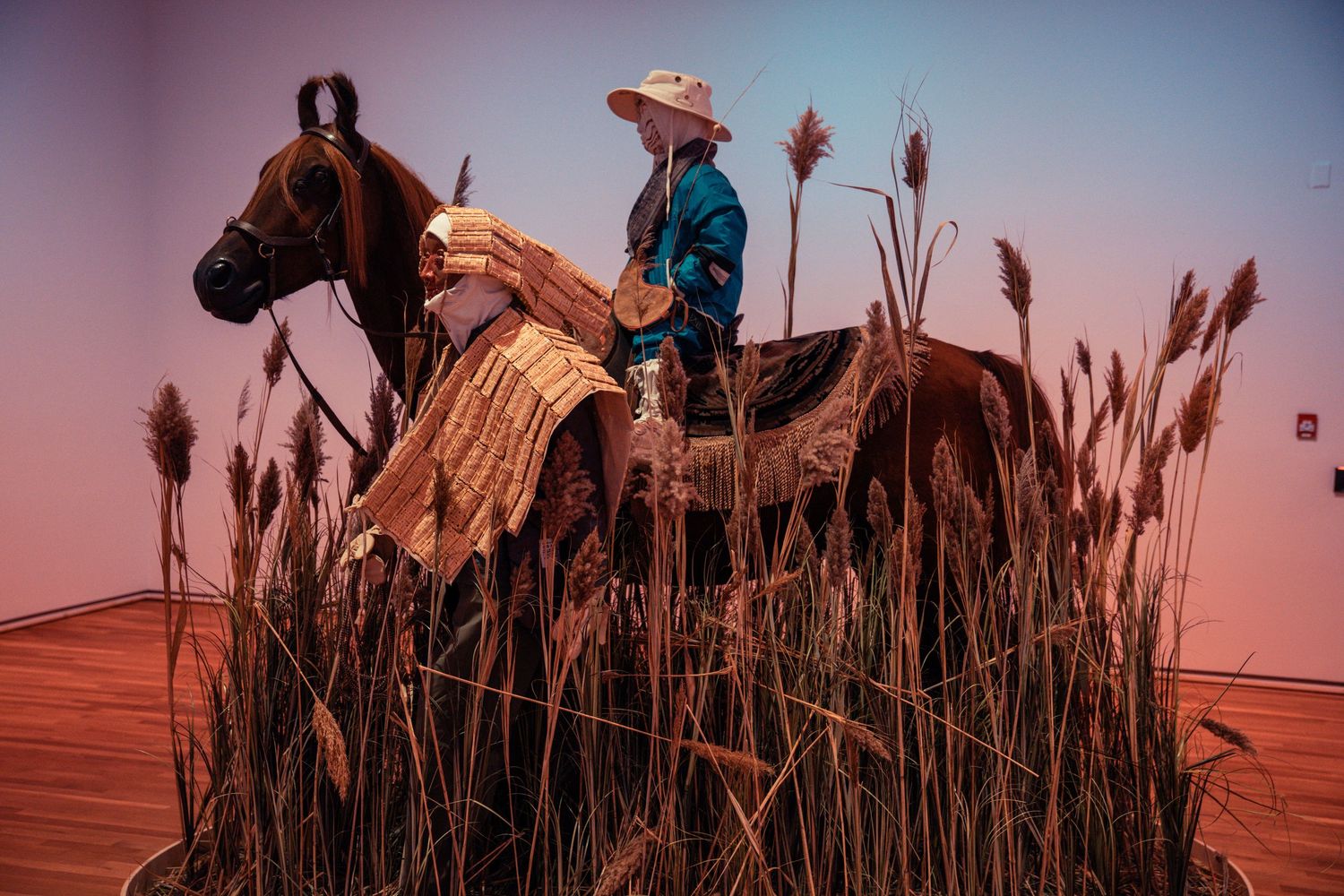 A rider on horseback stands among tall cattails against a dusky pink sky during sunset.