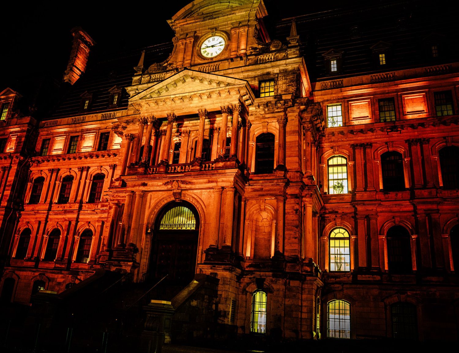 Historic building facade lit in dramatic orange lighting during nighttime.