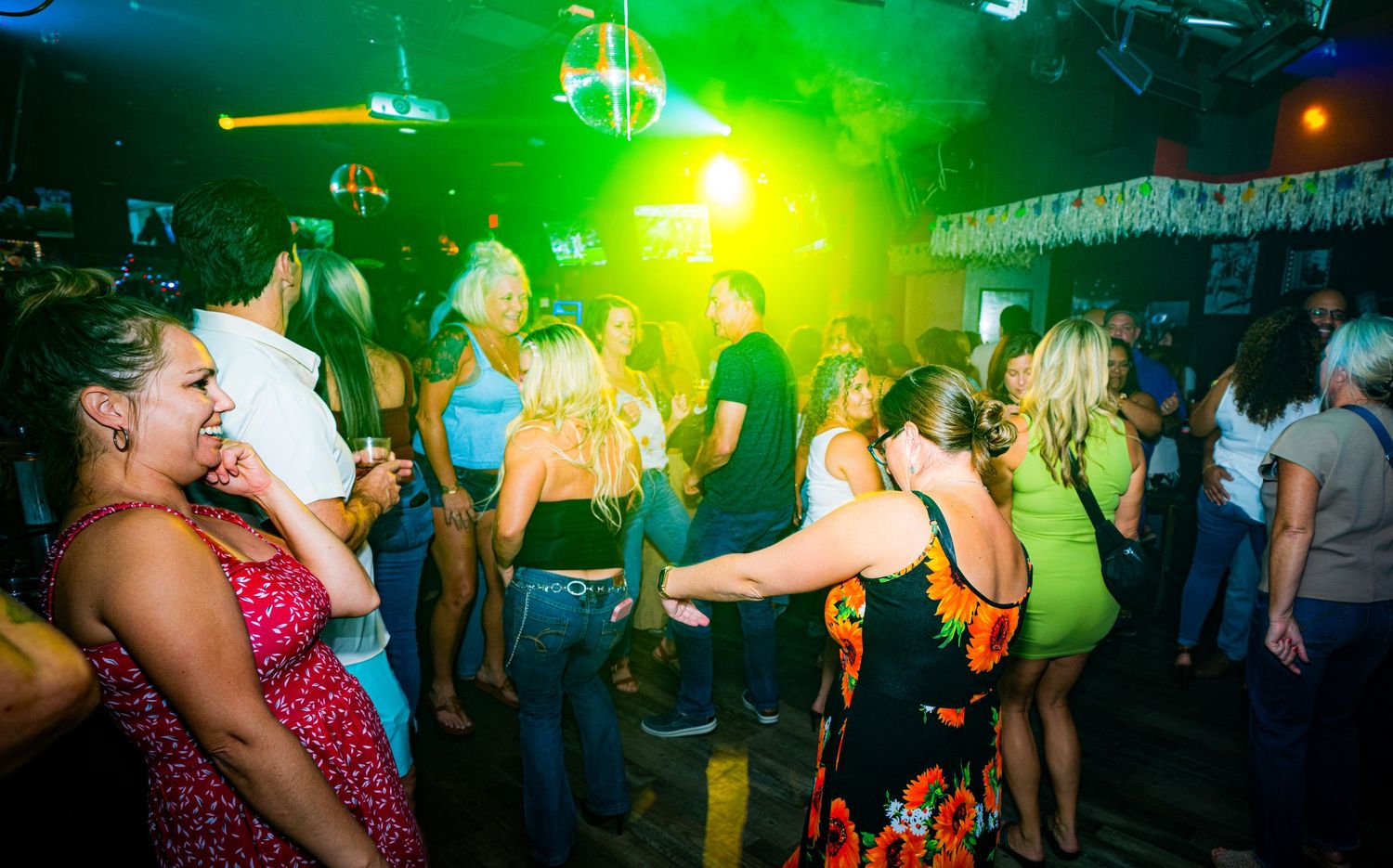 Dance floor illuminated by green lighting as party-goers dance and socialize.