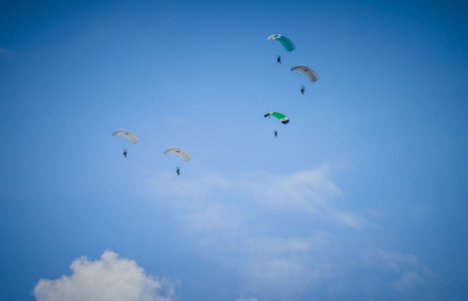 Multiple colorful parachutes floating against bright blue sky with white clouds.