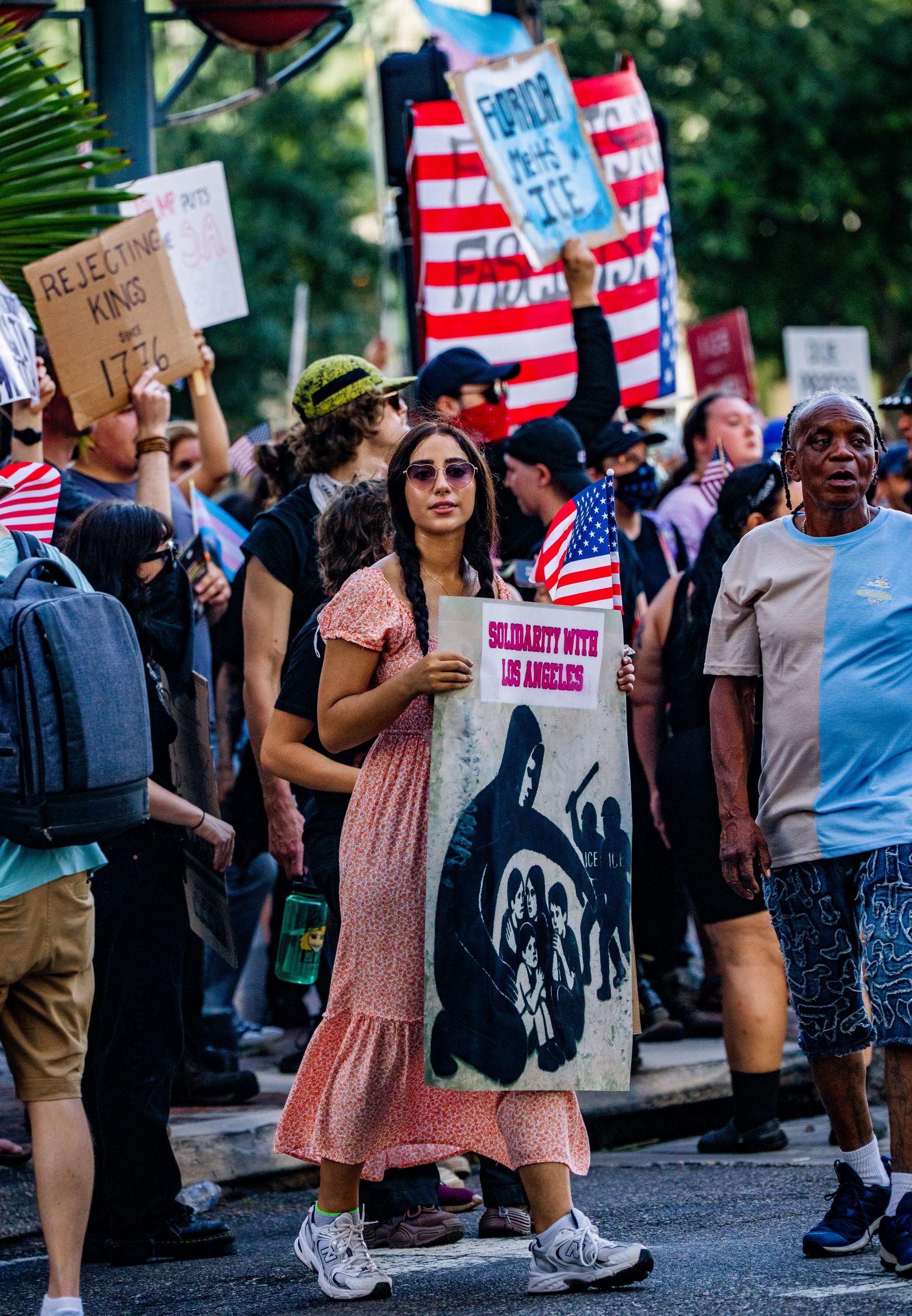 Crowd of protesters with American flags and signs gather at a street demonstration.