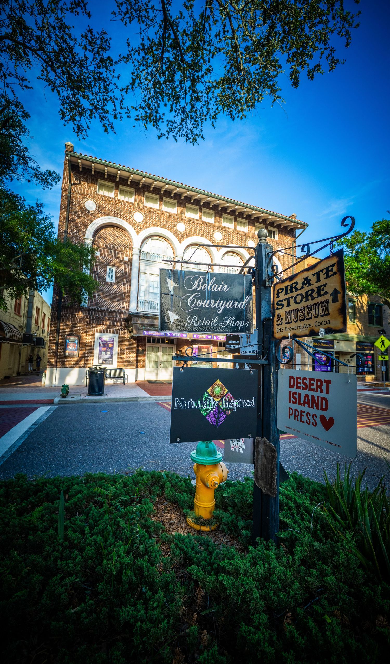 Vintage brick building storefront with decorative courtyard and retail shop signage against blue sky.
