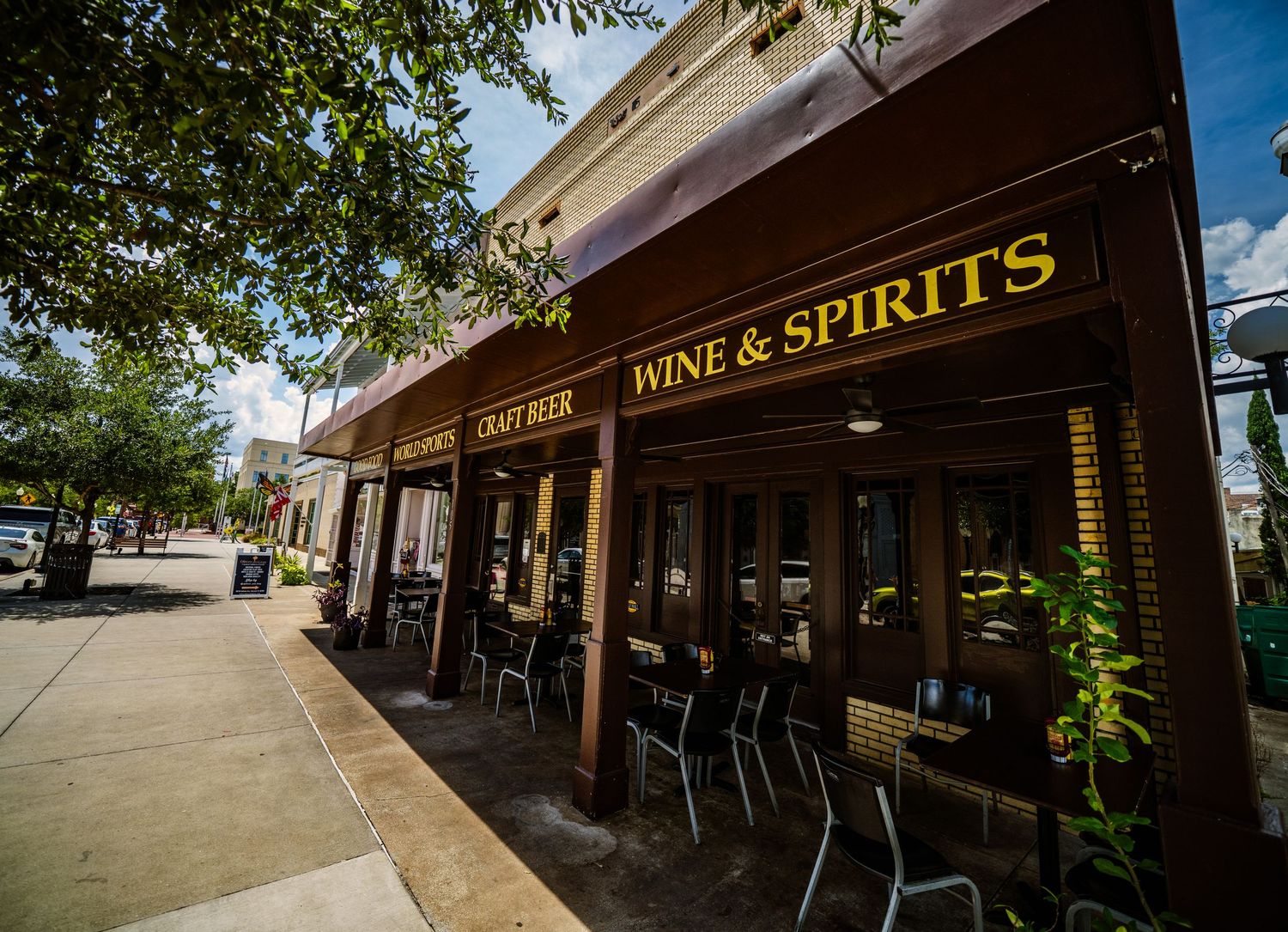 Wine and spirits store with outdoor seating area along a tree-lined street.