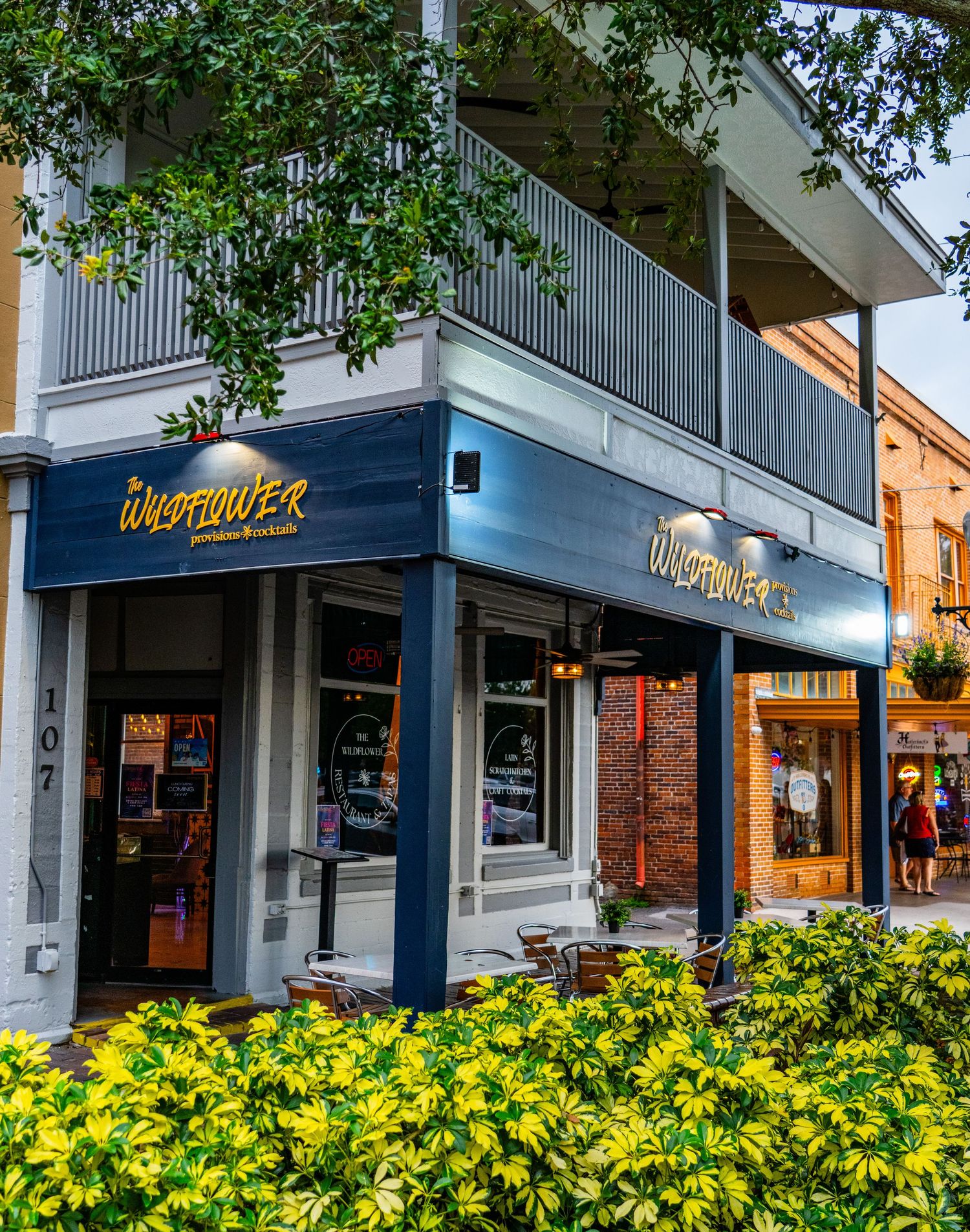 Blue-trimmed storefront of Uncle Maddox with yellow flowers blooming in landscaping below.