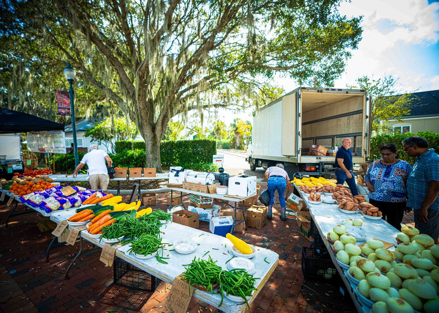 Fresh produce and goods displayed at an outdoor farmers market with colorful vegetables and tents on a sunny day.