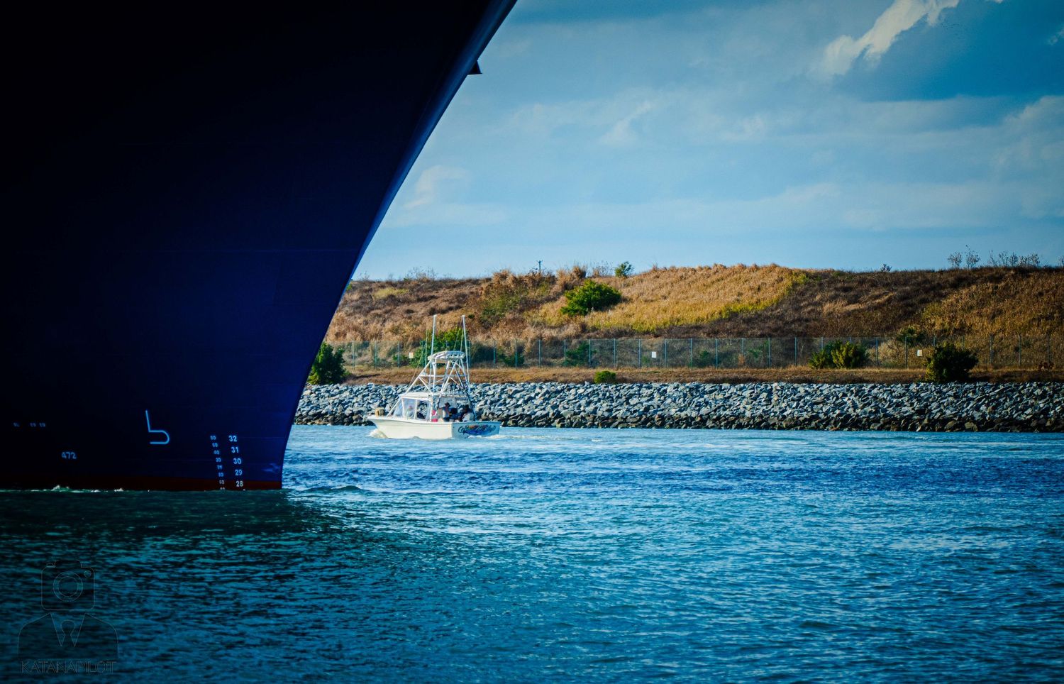 A panoramic sequence of blue ocean water with distant hills and boats in a marina under bright daylight.