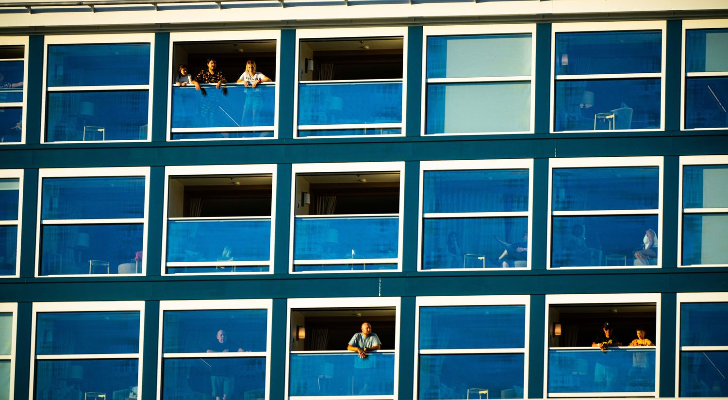 Modern office building exterior with rows of blue tinted glass windows reflecting sunlight across the facade.