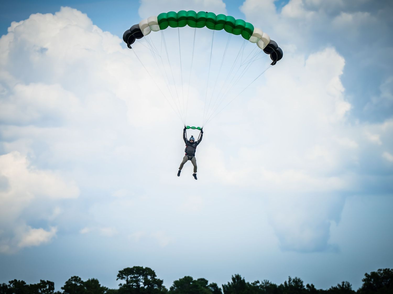 Silhouette of parachutist descending against a bright cloudy sky background.