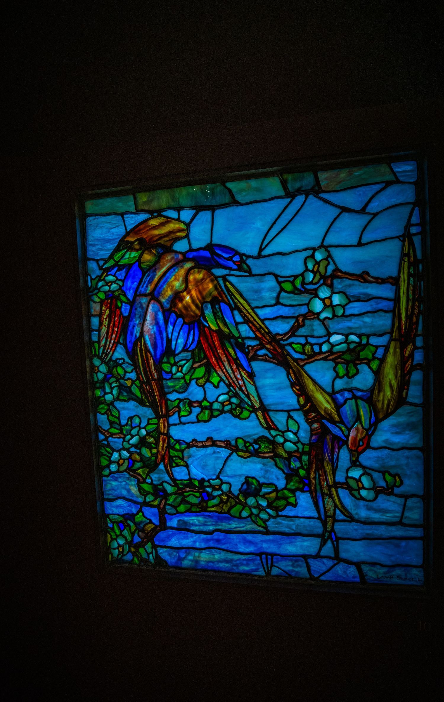 Stained glass window depicting colorful birds among flowering vines against a deep blue background.