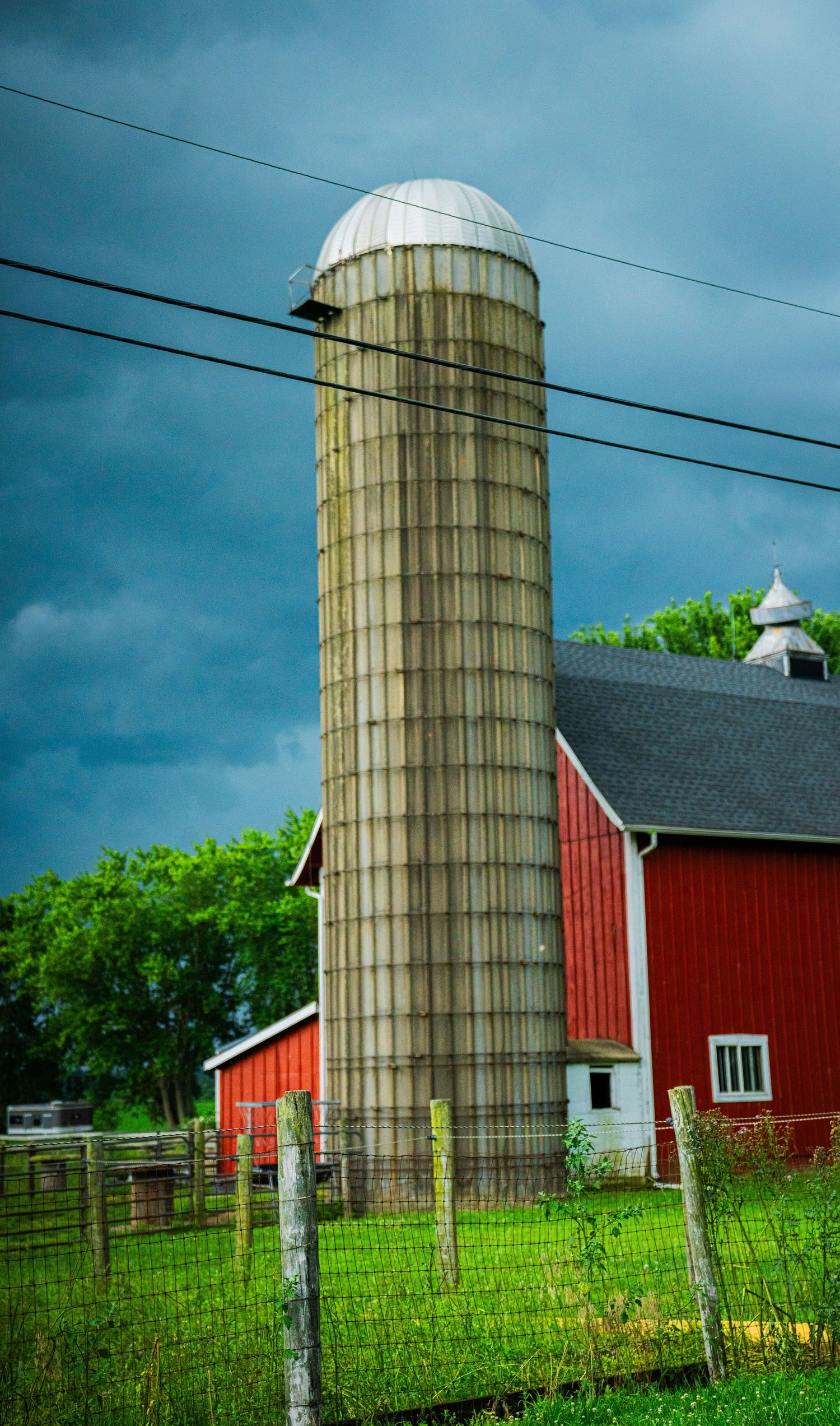 Tall concrete silo stands next to a classic red barn against a stormy blue sky.