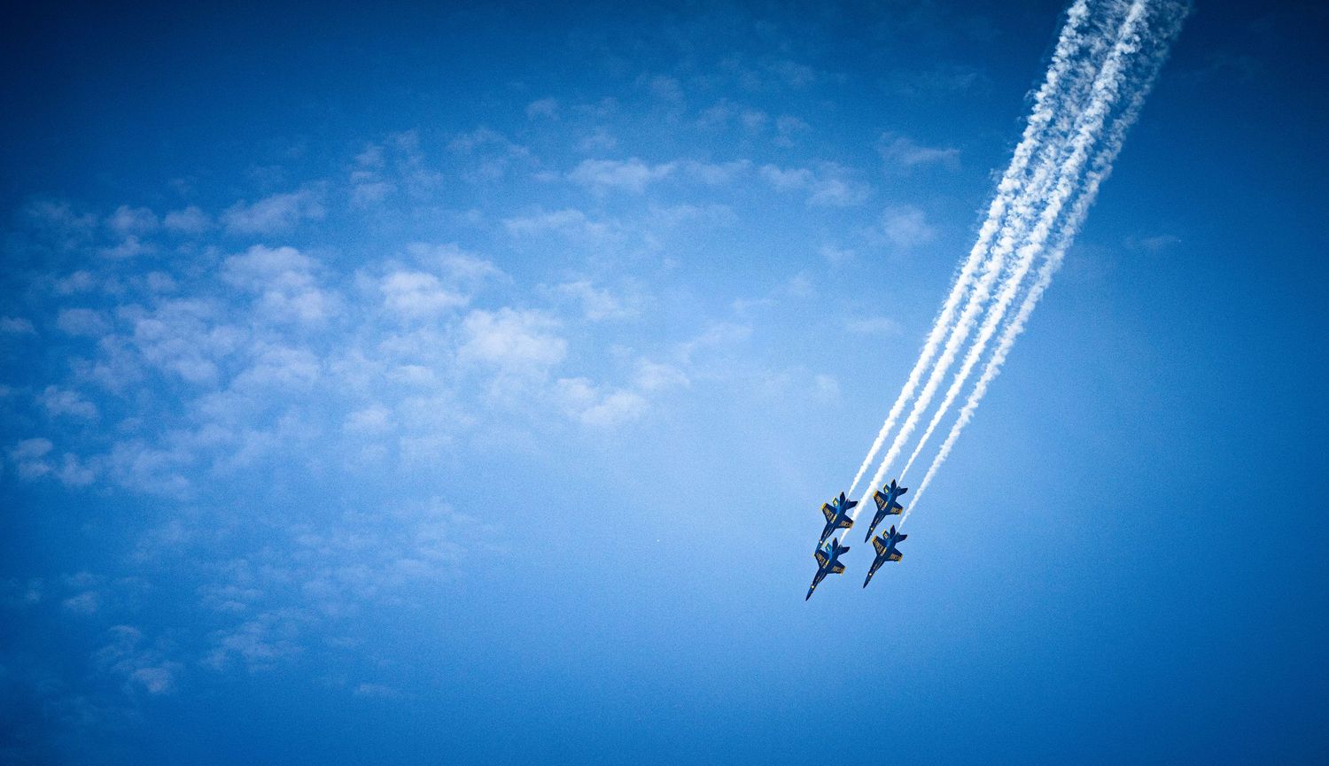 Fighter jets perform synchronized flight maneuvers leaving white vapor trails in bright blue sky.