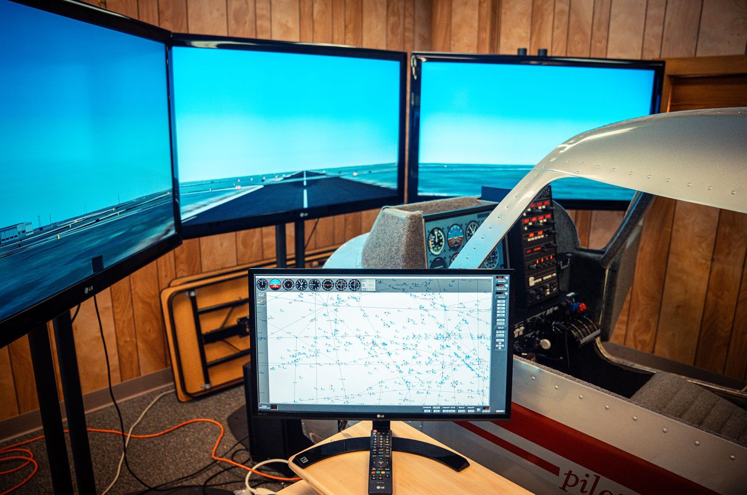 Wide-angle view of a home flight simulator with wooden paneled walls and blue sky displays.