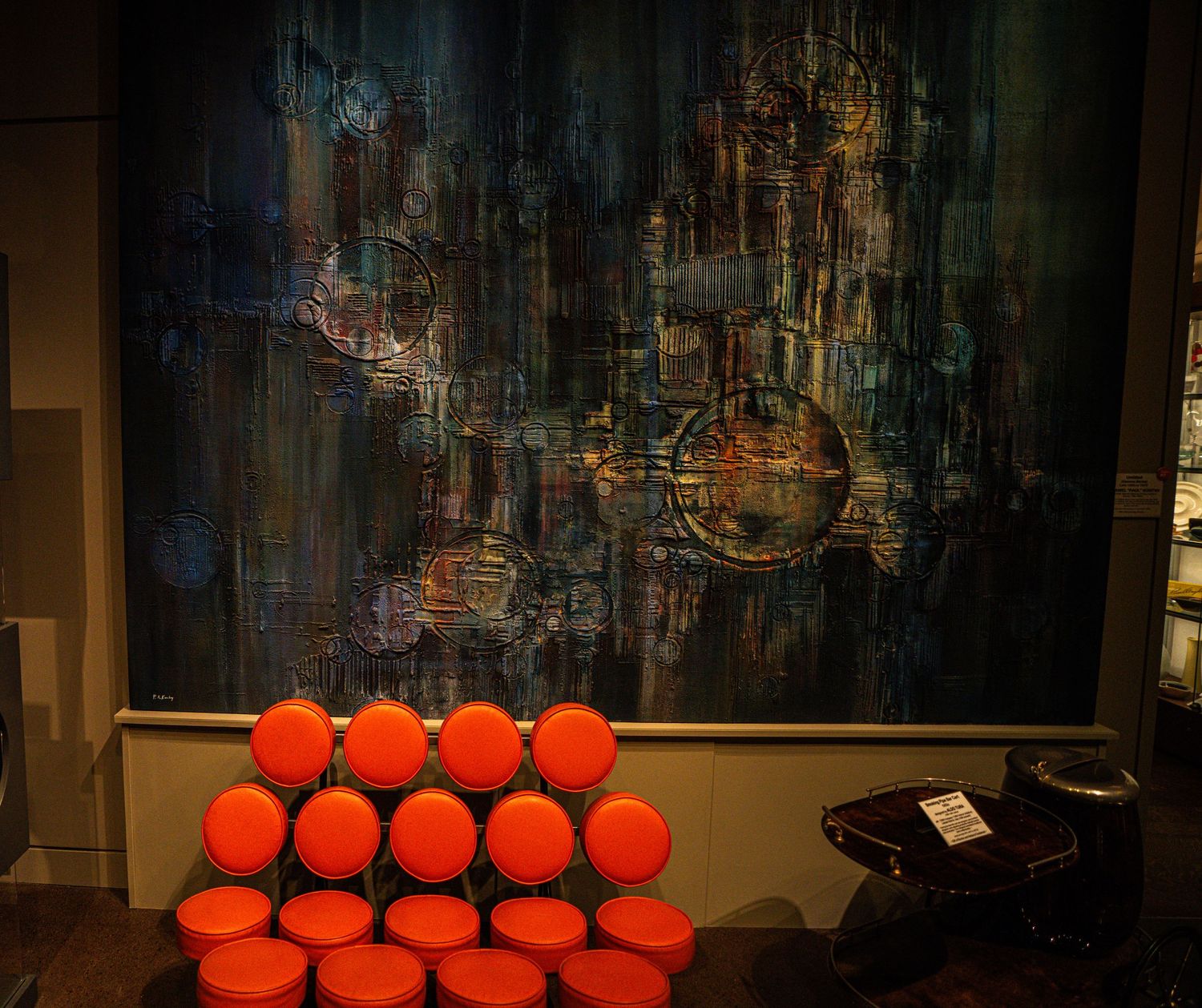 Orange spherical cushions arranged in a pyramid shape against a dark abstract painting in a modern interior setting.