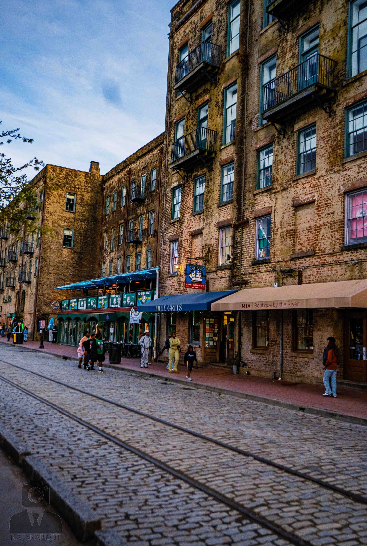 Historic brick building with shops along a cobblestone street in Savannah's River Street district.