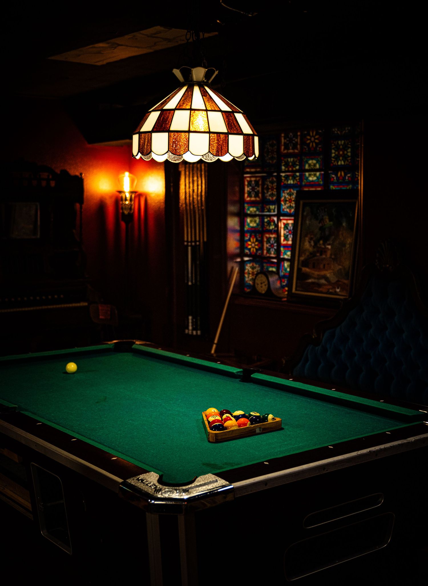 A dimly lit pool table with Tiffany-style hanging lamps creates a moody billiards room ambiance.