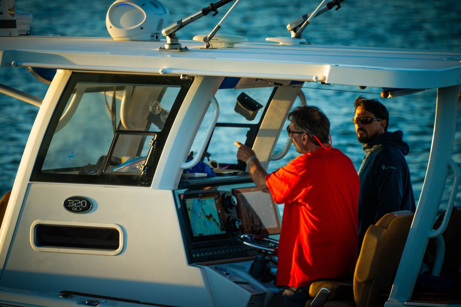 Two people operate navigation equipment inside the cabin of a fishing boat on blue waters.