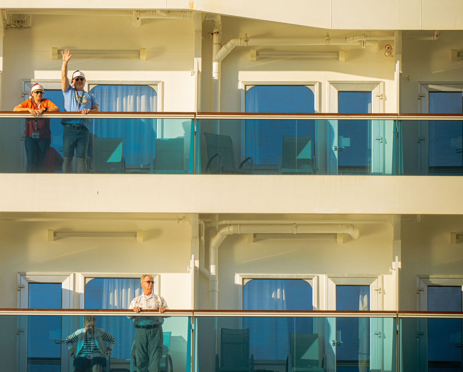 Cruise ship balconies with blue glass panels and white railings showing passengers enjoying the ocean view.