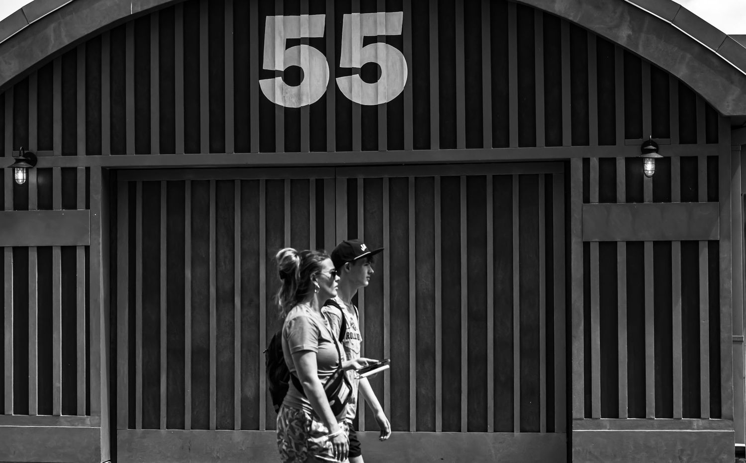 A black and white film strip sequence showing a person walking past vertical bars or pillars in an architectural setting.